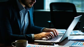 A business person is intently focused on their laptop fingers deftly typing away as they navigate through spreadsheets and emails The dimly lit office-1