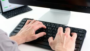 person working on computer you see their hands typing on the keyboard and you dont see the screen